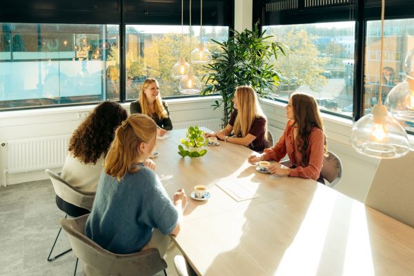 Een teamoverleg met 5 mensen aan een grote lange tafel.